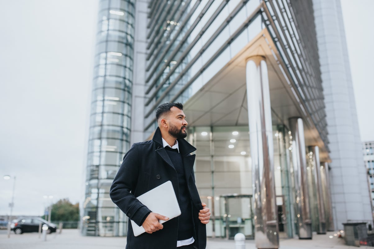 Contemplative ethnic entrepreneur with laptop near modern urban building